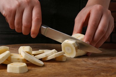 Woman cutting delicious fresh ripe parsnip at wooden board, closeup