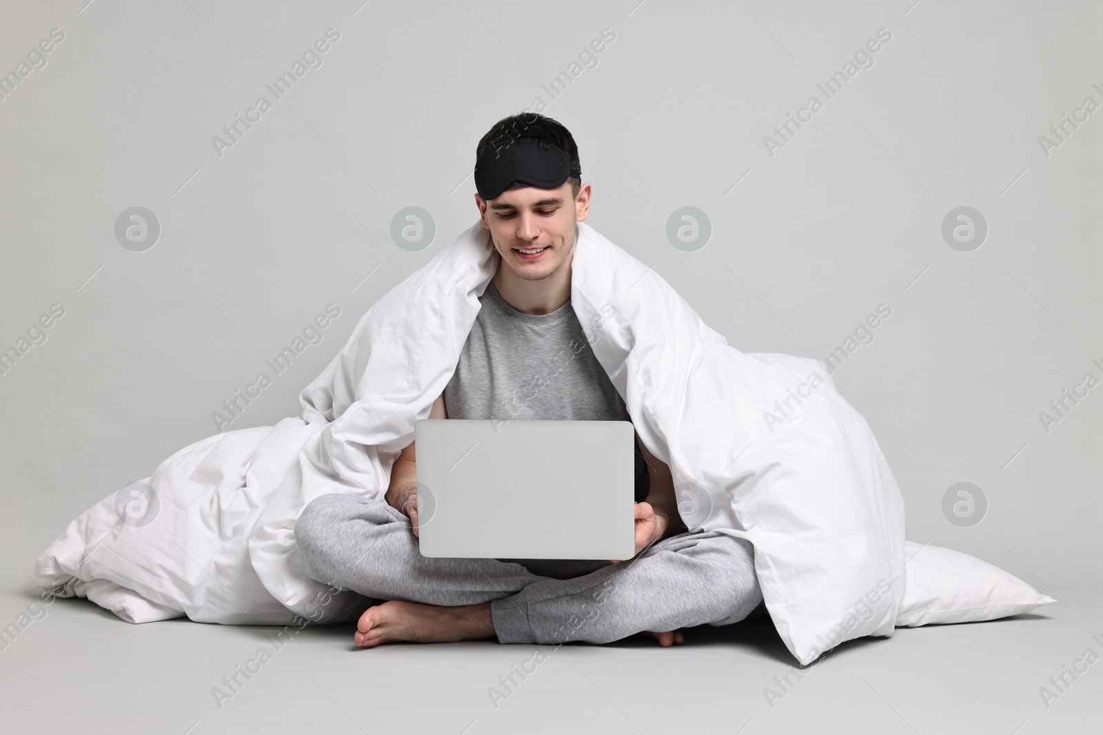Photo of Happy man in pyjama wrapped in blanket using laptop on grey background