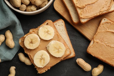 Photo of Tasty peanut butter sandwiches with sliced banana and peanuts on dark gray table, flat lay