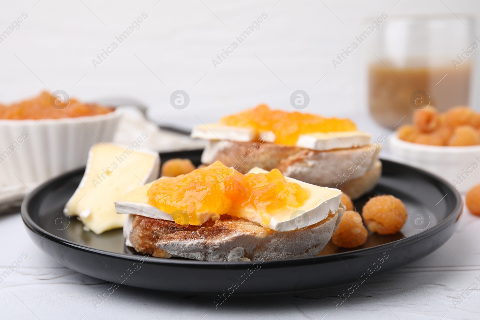 Photo of Tasty sandwiches with brie cheese, fresh raspberry and apricot jam on white table, closeup