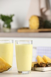 Glasses of tasty pineapple smoothie and cut fruit on white table indoors