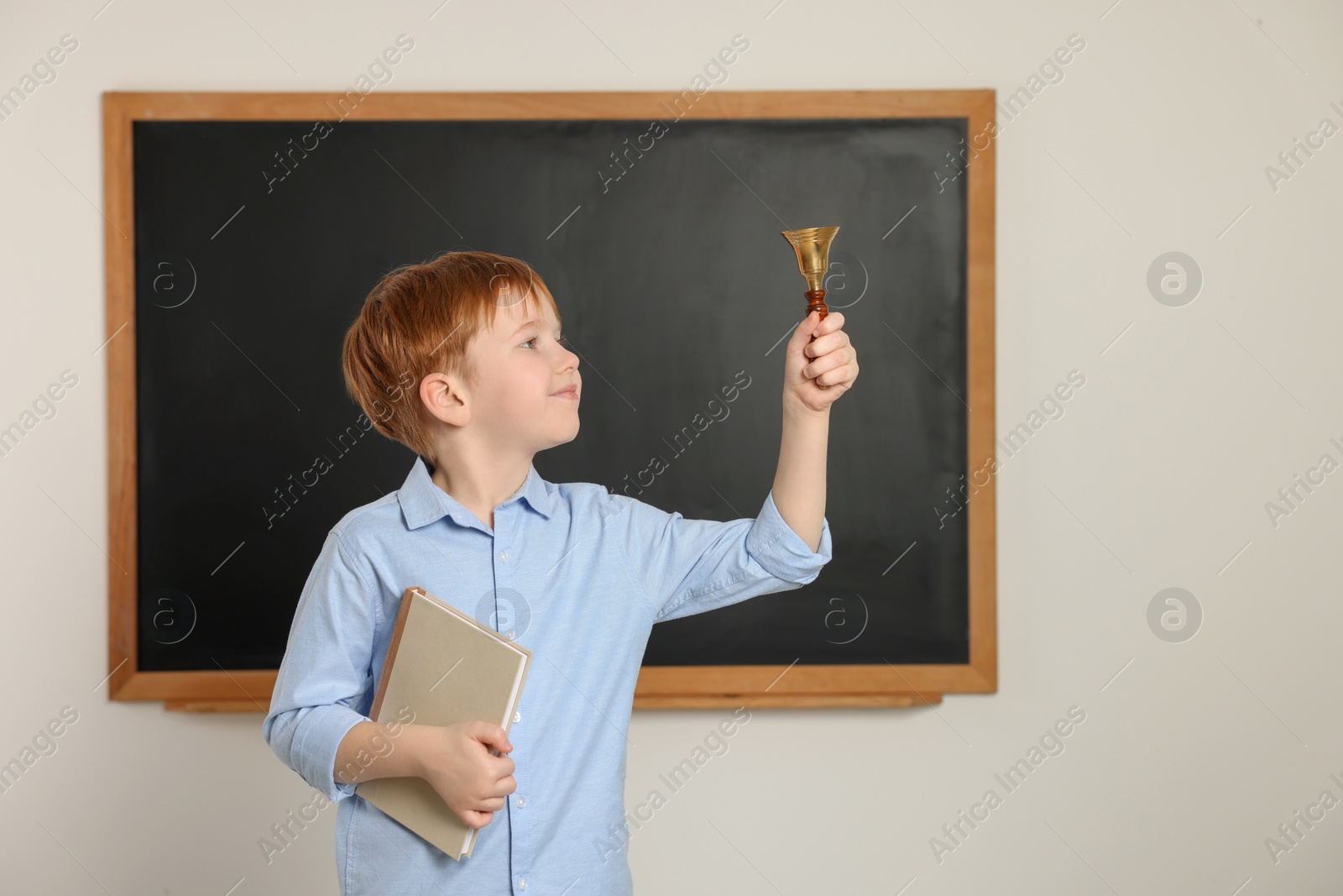 Photo of Cute little boy ringing school bell in classroom