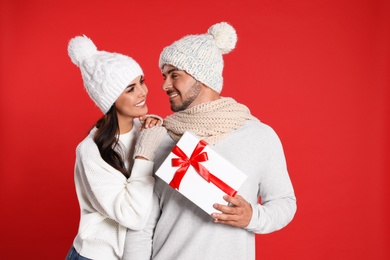 Lovely young couple with gift box on red background. Christmas celebration