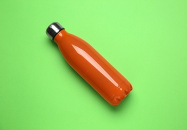 Photo of New modern thermo bottle on green background, top view