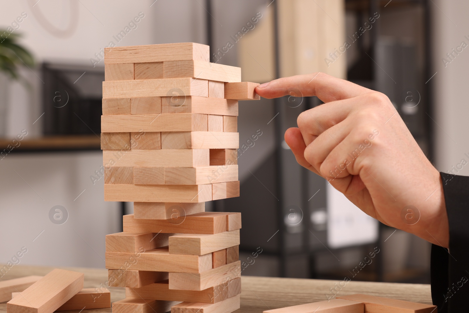 Photo of Playing Jenga. Man building tower with wooden blocks at table, closeup