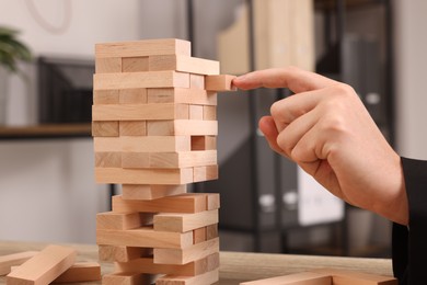 Playing Jenga. Man building tower with wooden blocks at table, closeup