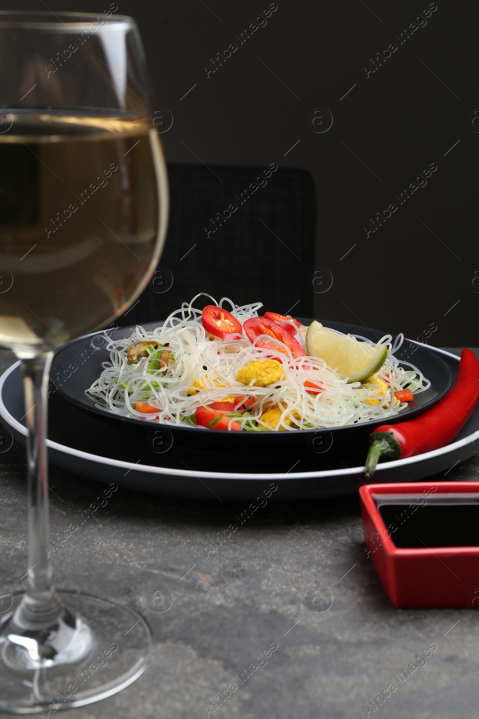 Photo of Stir-fry. Tasty rice noodles with meat and vegetables served on grey textured table