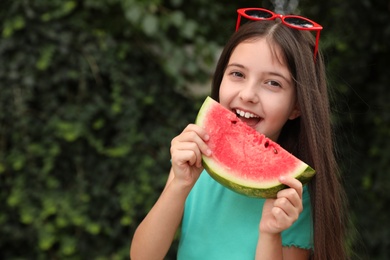 Photo of Cute little girl eating watermelon outdoors on sunny day