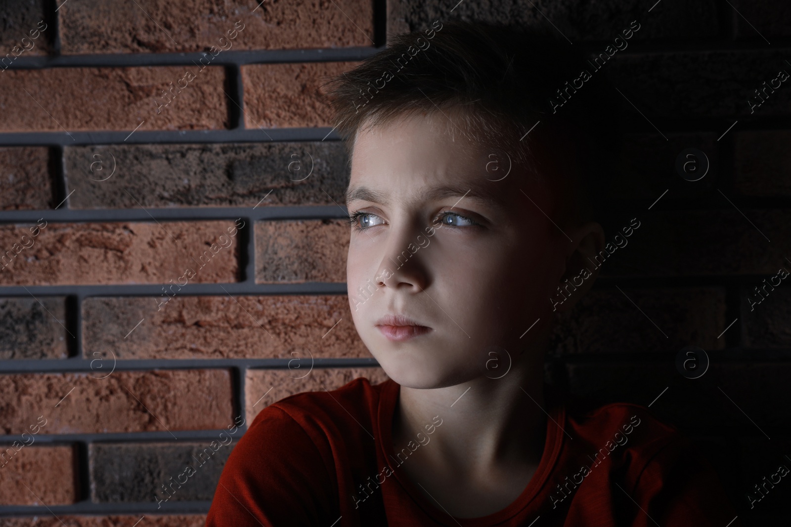 Photo of Sad little boy near brick wall. Domestic violence concept