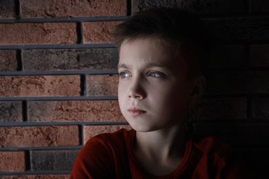 Photo of Sad little boy near brick wall. Domestic violence concept