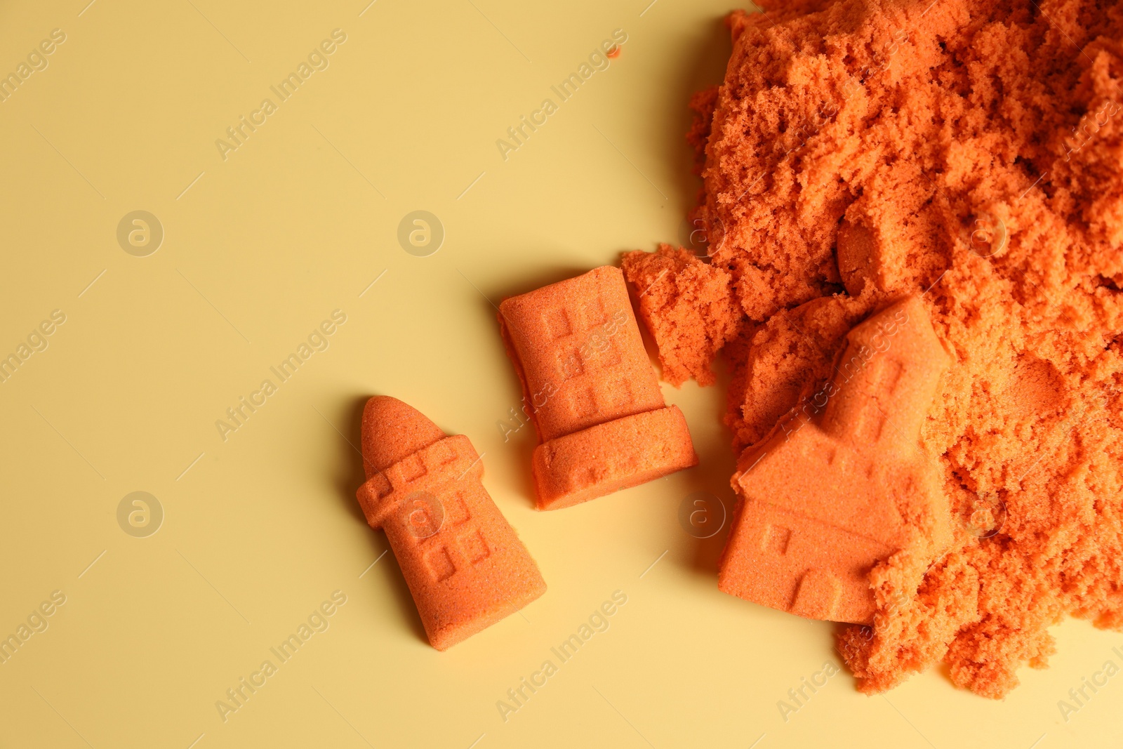 Photo of Castle figures made of orange kinetic sand on beige background, flat lay. Space for text