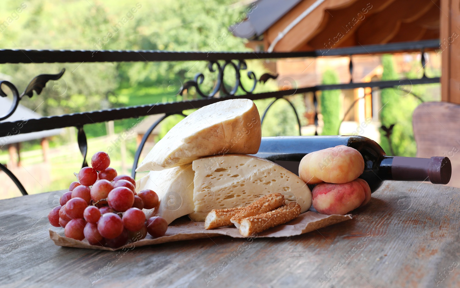 Photo of Delicious cheese, ripe grape, peaches and bottle of wine on wooden table