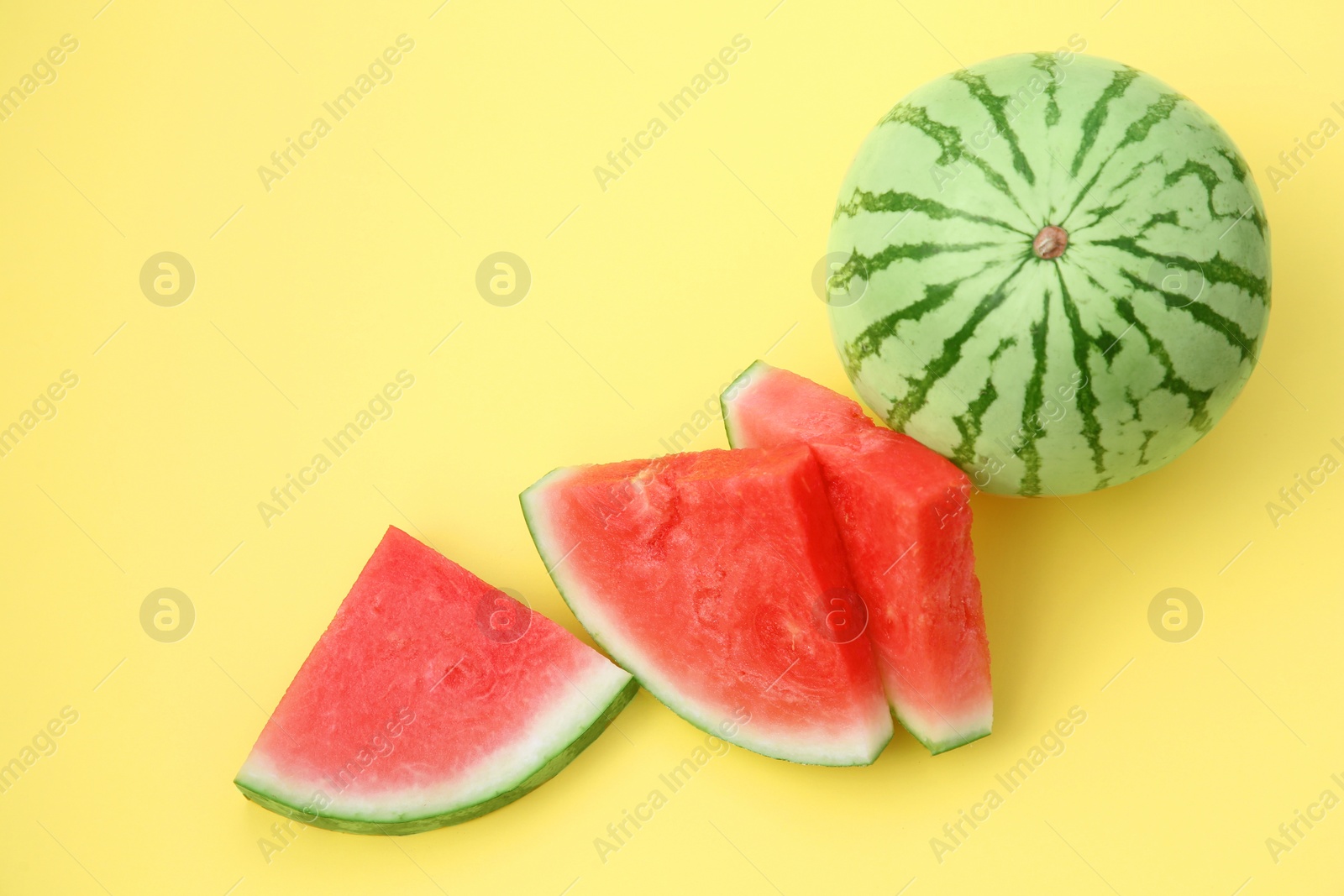 Photo of Delicious cut and whole ripe watermelons on yellow background, flat lay. Space for text