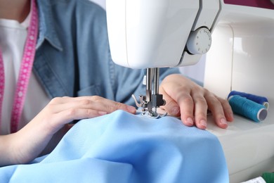 Photo of Seamstress working with sewing machine at table indoors, closeup