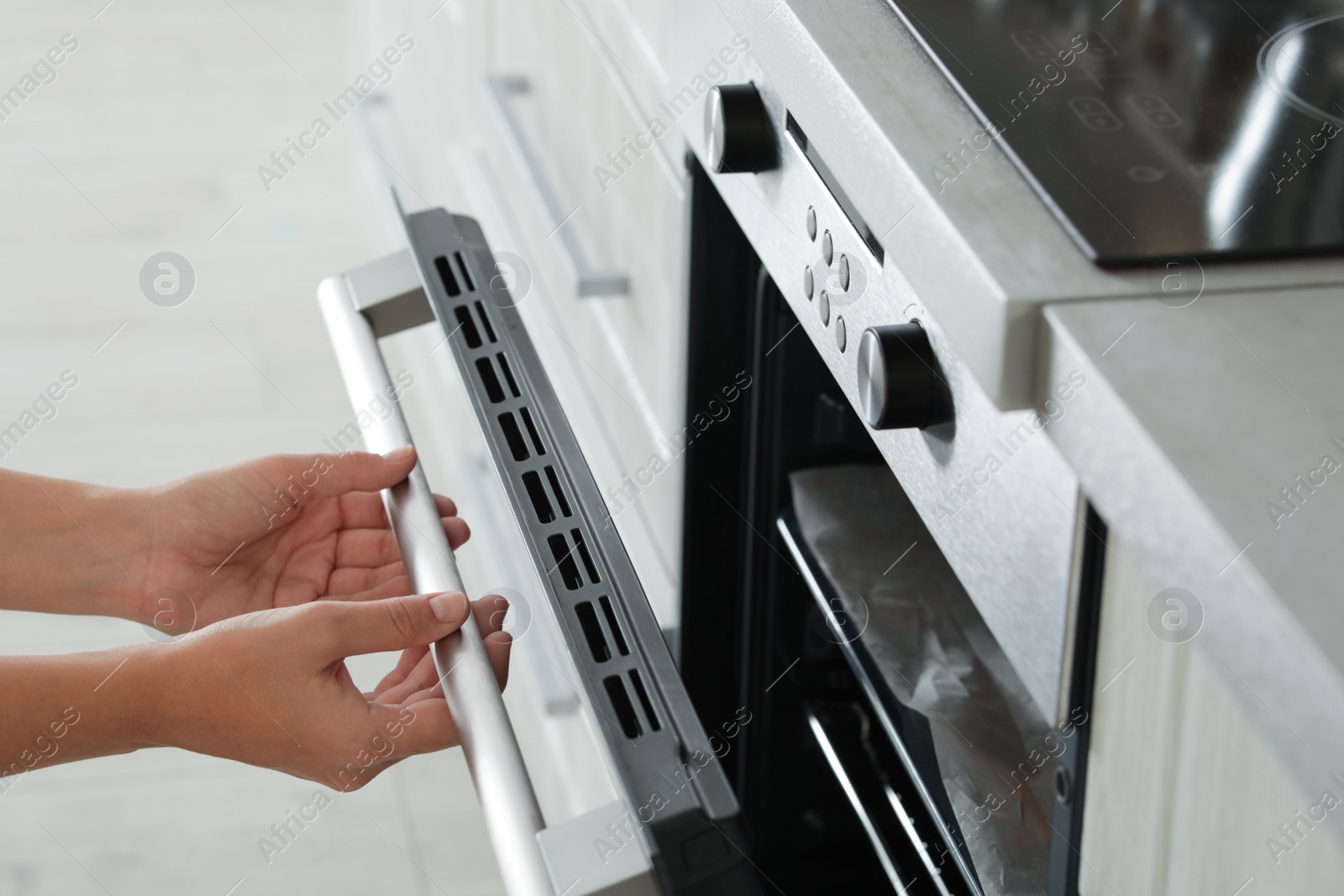 Photo of Young woman opening electric oven in kitchen, closeup