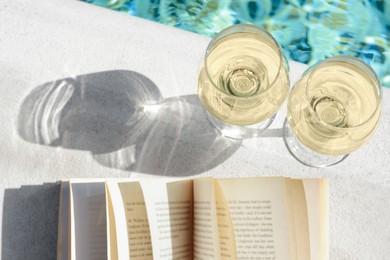 Glasses of tasty wine and open book on swimming pool edge, above view