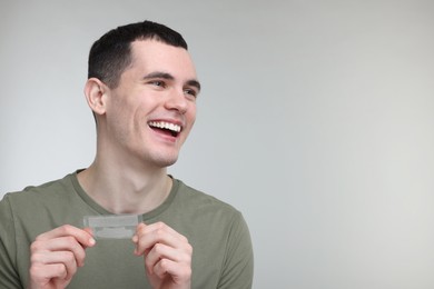 Photo of Young man with whitening strips on light grey background. Space for text