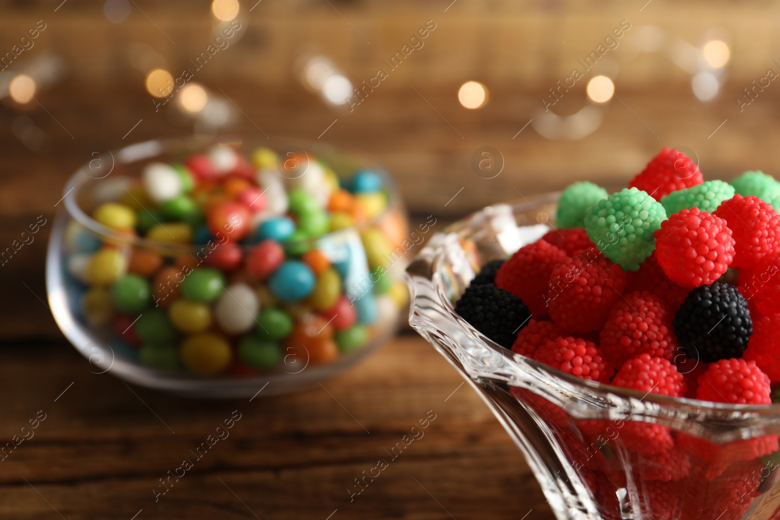 Photo of Delicious jelly candies in bowl on wooden table, closeup. Space for text