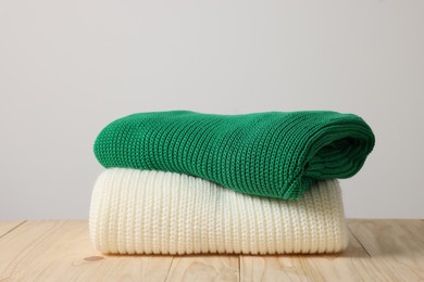 Folded knitted sweaters on wooden table against light background