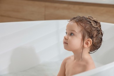 Photo of Cute little girl washing hair with shampoo in bathroom. Space for text
