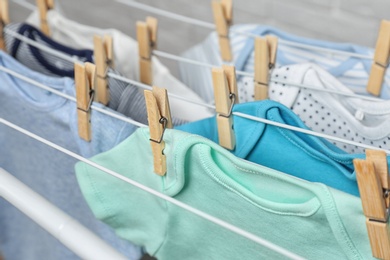 Photo of Different cute baby onesies hanging on clothes line, closeup. Laundry day