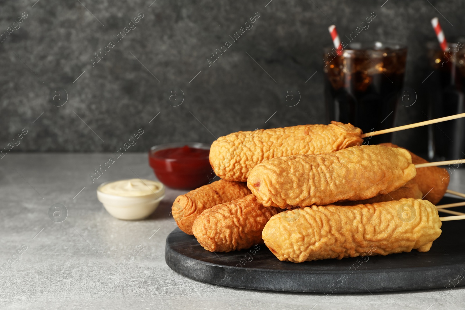 Photo of Delicious deep fried corn dogs with board and sauces on light grey table. Space for text