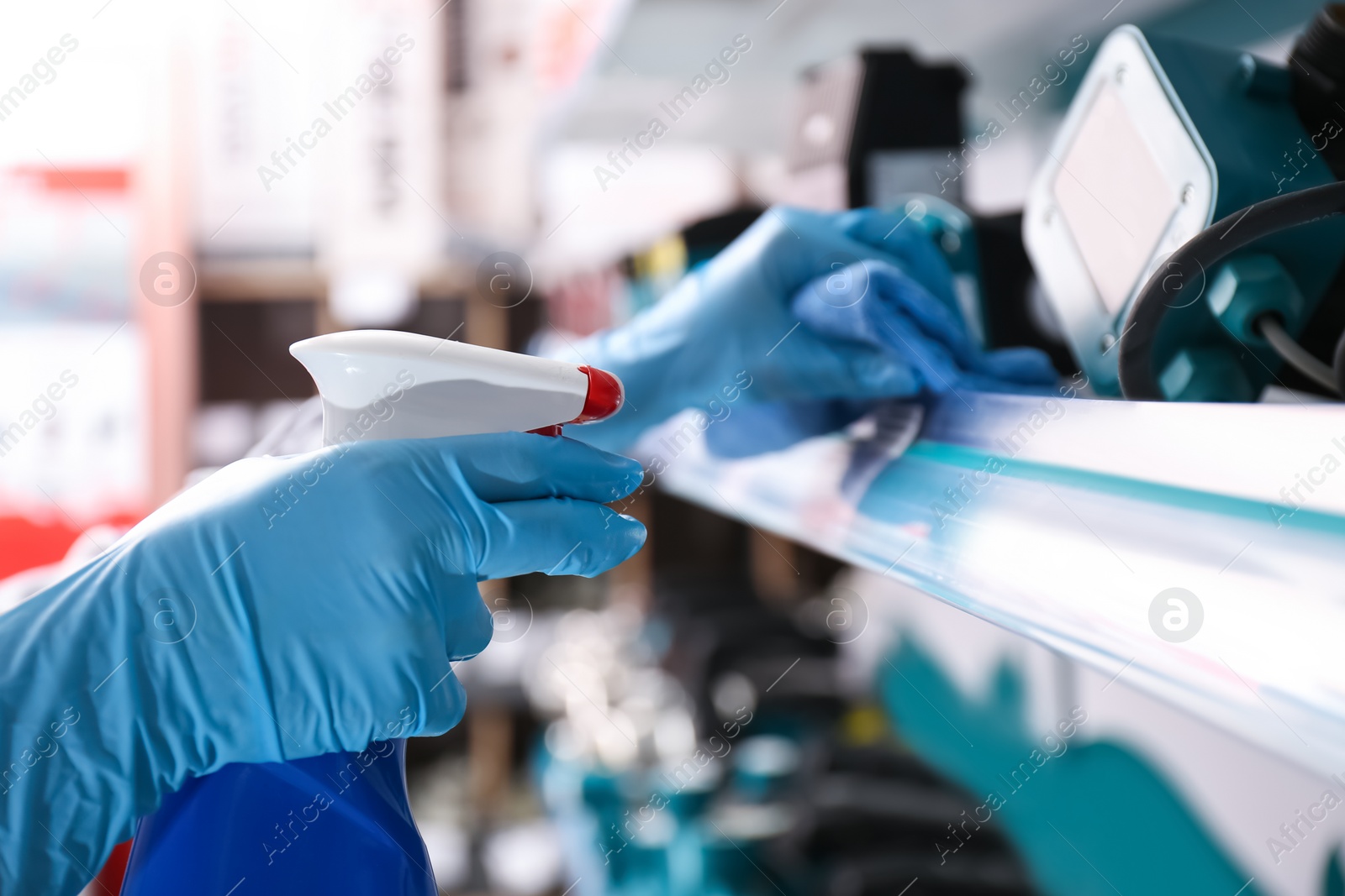 Photo of Woman cleaning shelf with rag and detergent in store, closeup