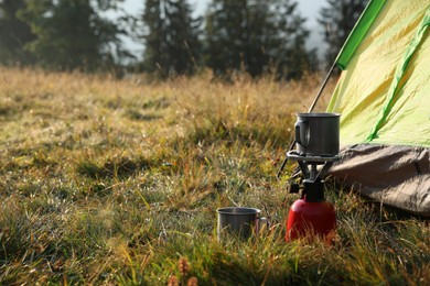 Photo of Portable gas burner with cup near camping tent in mountains. Space for text