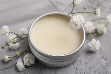 Photo of Lip balm and gypsophila flowers on grey textured table, closeup
