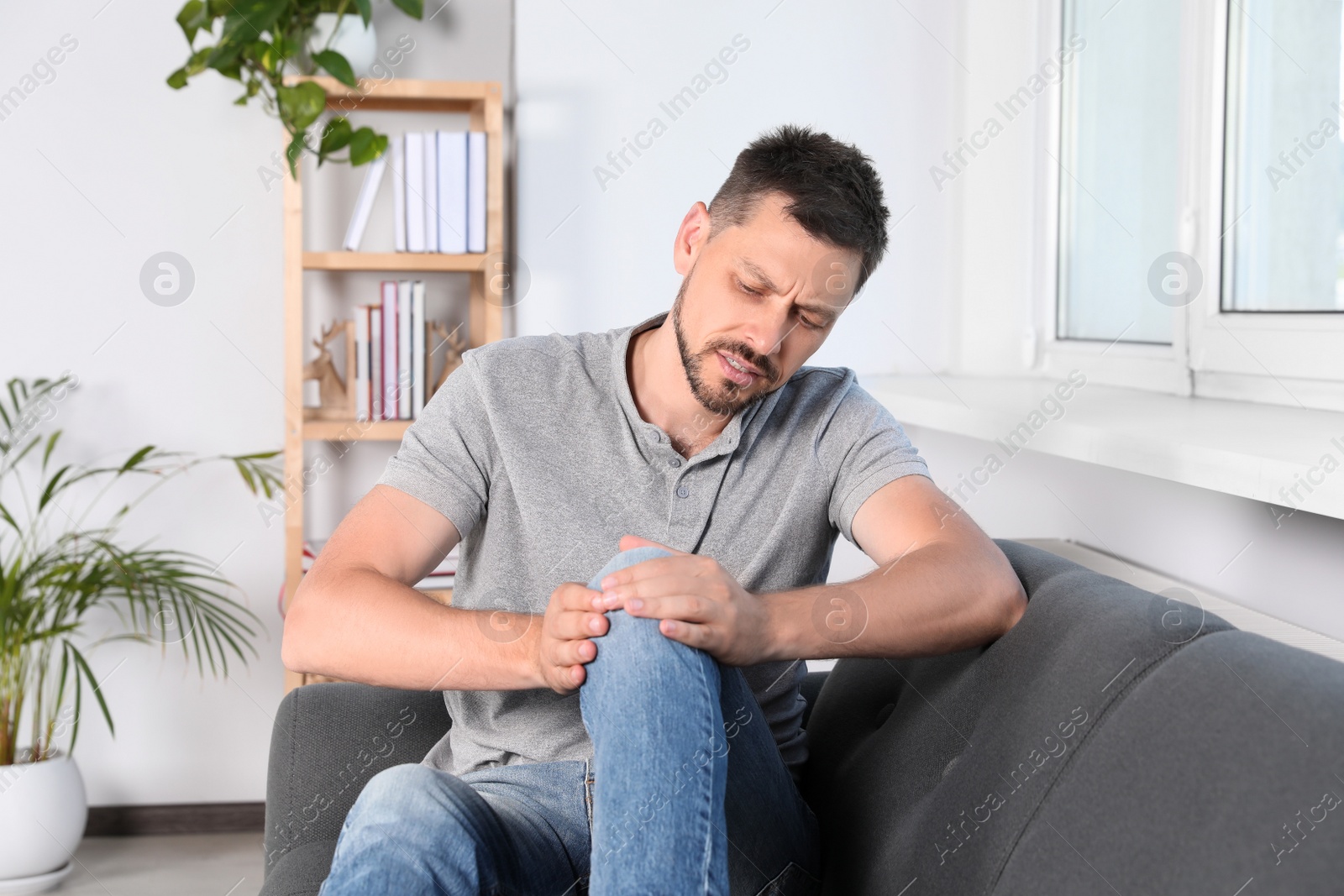 Photo of Man suffering from knee pain on sofa at home