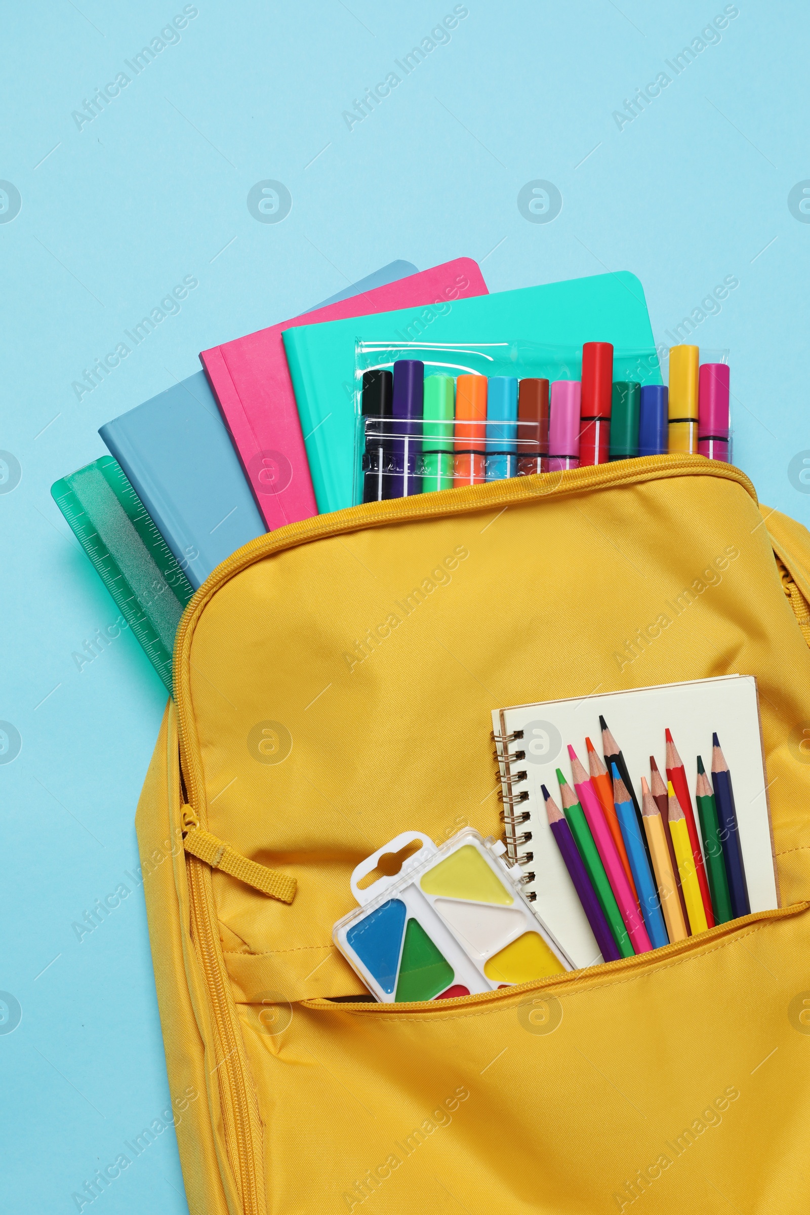 Photo of Backpack with different school stationery on light blue background, top view