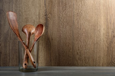 Photo of Set of wooden kitchen utensils in glass holder on grey table. Space for text