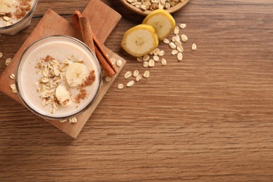 Photo of Tasty banana smoothie with oatmeal and cinnamon on wooden table, flat lay. Space for text