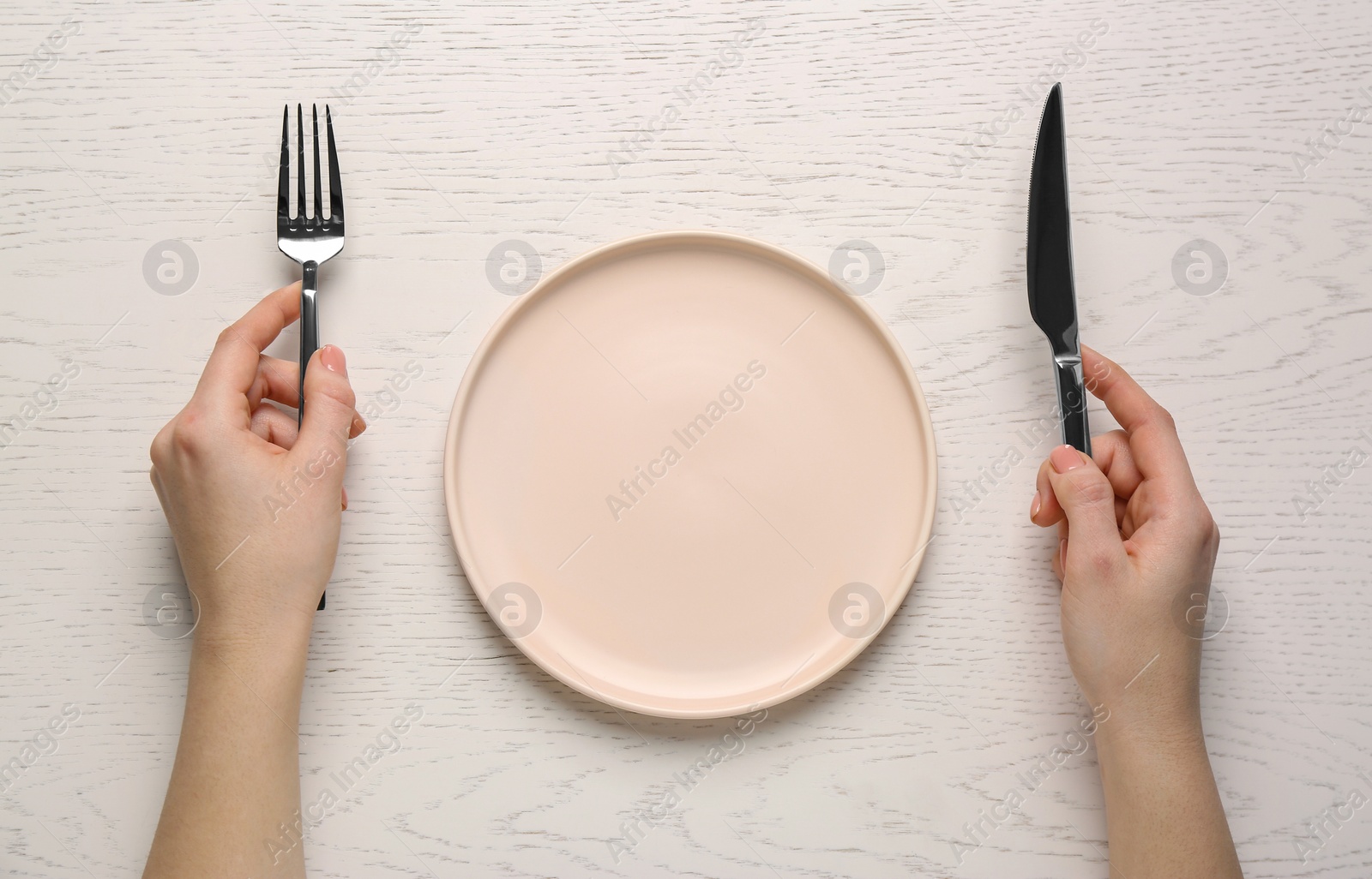 Photo of Woman with empty plate and cutlery at white wooden table, top view