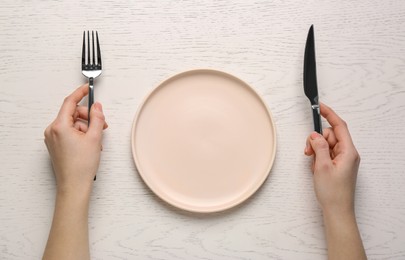 Woman with empty plate and cutlery at white wooden table, top view