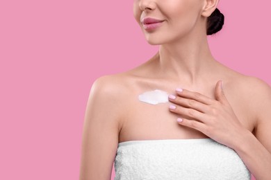 Photo of Woman with smear of body cream on her chest against pink background, closeup. Space for text