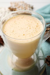 Photo of Glass cup with tasty eggnog on table, closeup