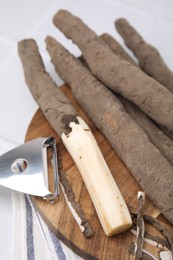 Raw salsify roots and peeler on white table