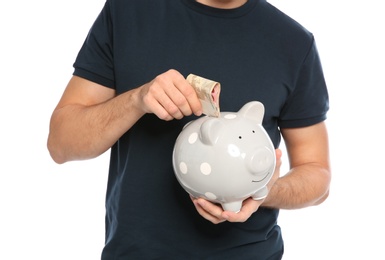 Photo of Young man putting money into piggy bank on white background, closeup