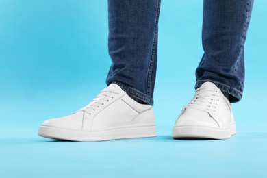 Photo of Man wearing stylish white sneakers on light blue background, closeup