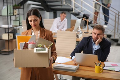 Photo of Upset dismissed young woman carrying box with stuff in office