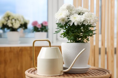 Photo of Beautiful chrysanthemum plant in flower pot and watering can on wooden table indoors. Space for text
