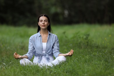 Photo of Young woman meditating on green grass. Space for text