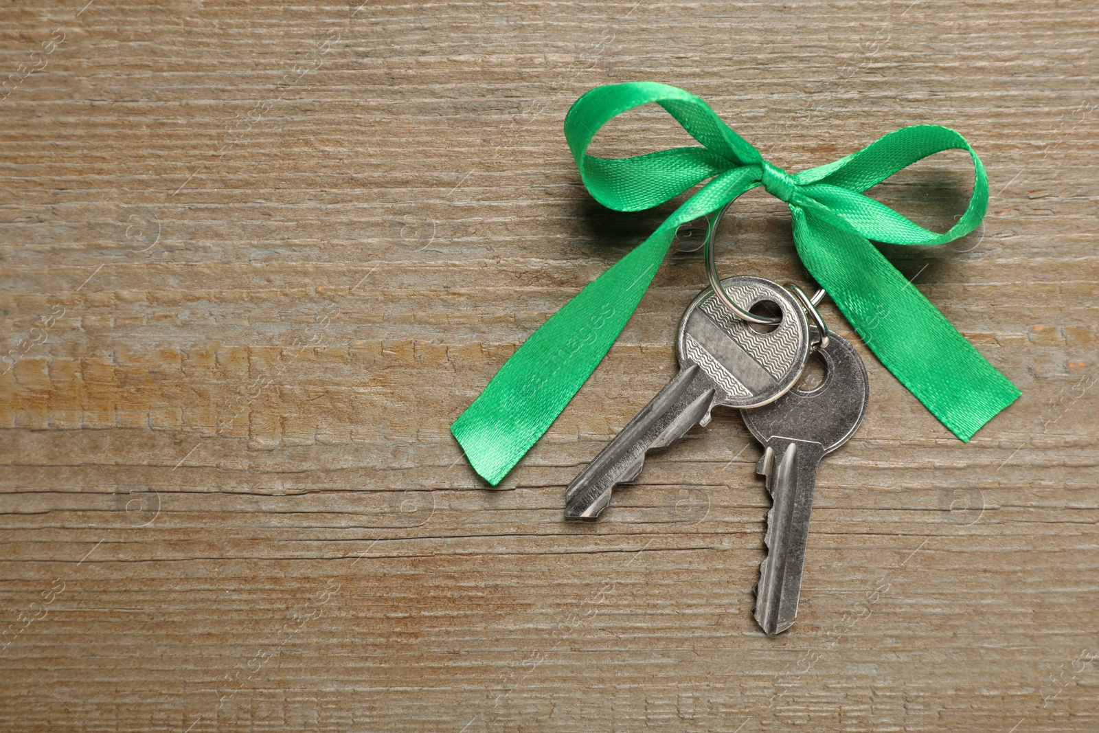 Photo of Keys with green bow on wooden table, top view and space for text. Housewarming party