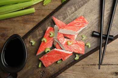 Photo of Fresh crab sticks with celery and soy sauce served on wooden table, flat lay