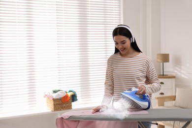 Young woman ironing clothes with steam at home. Space for text