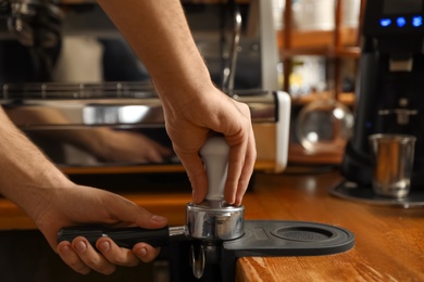 Barista tamping coffee in portafilter at bar counter, closeup. Space for text