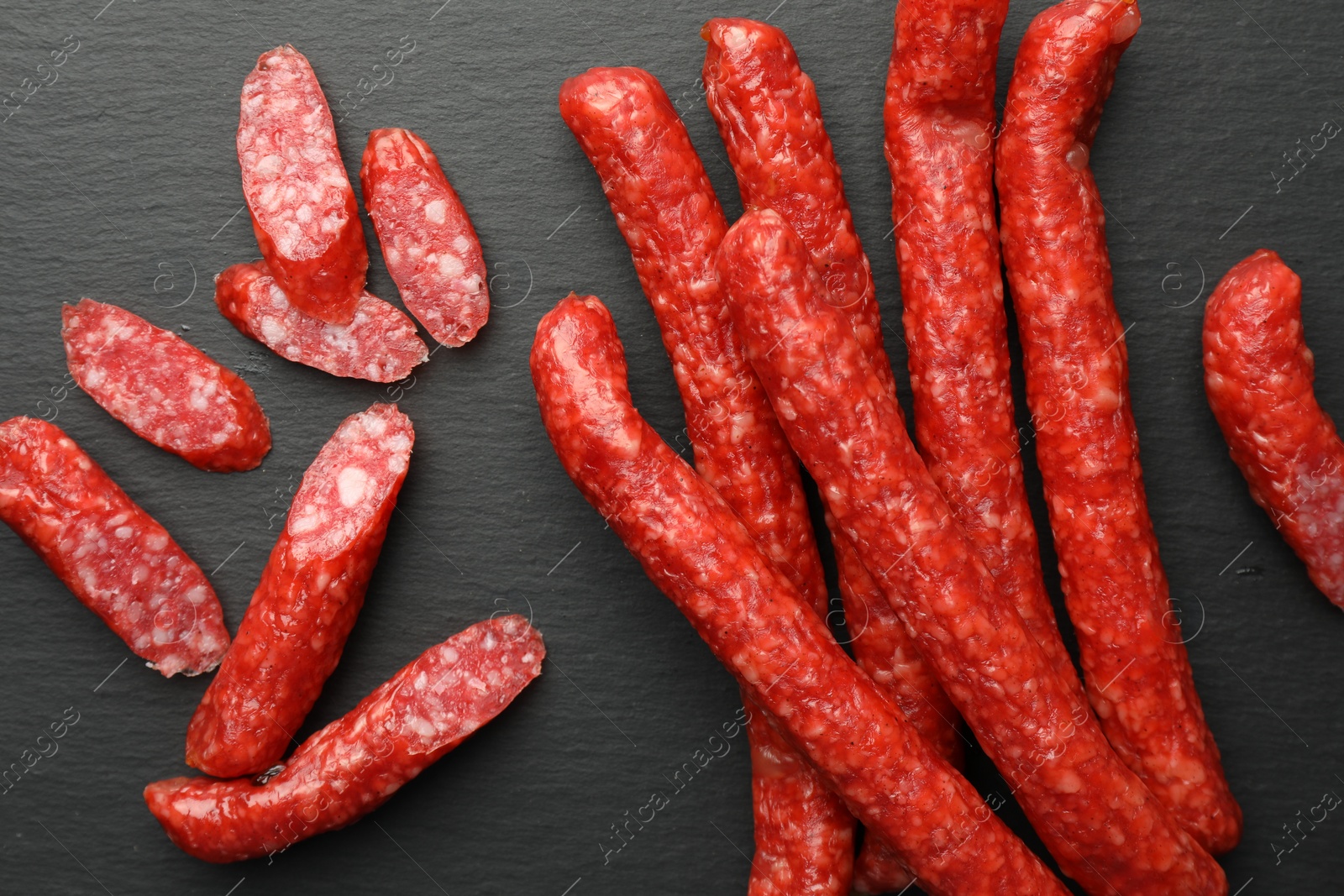 Photo of Many thin dry smoked sausages on black table, flat lay