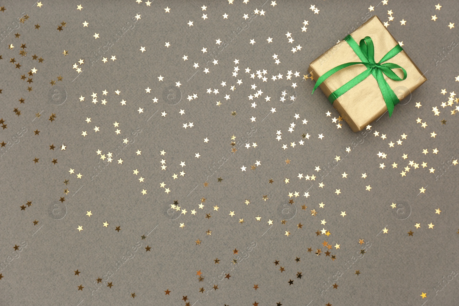 Photo of Golden gift box and shiny confetti on grey background, top view. Space for text