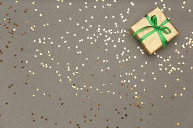 Photo of Golden gift box and shiny confetti on grey background, top view. Space for text